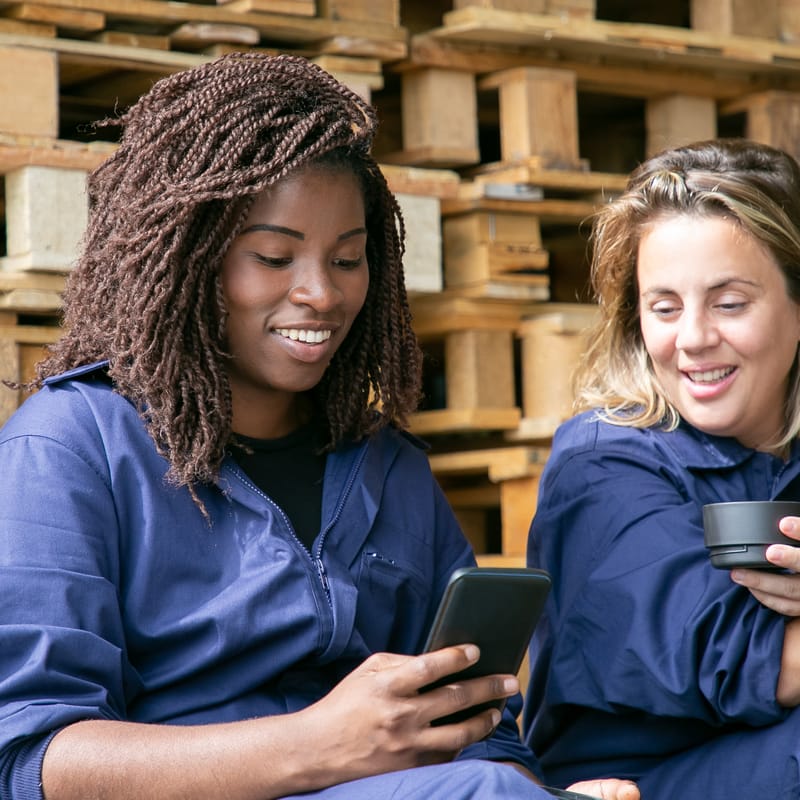 Two women at work looking at a phone, drinking coffee and chatting in English.