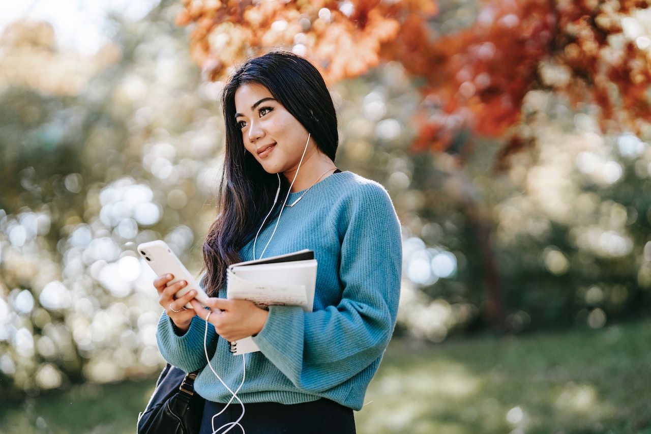 Woman in nature listening to audiobooks on a headphone to learn how to pronounce English words