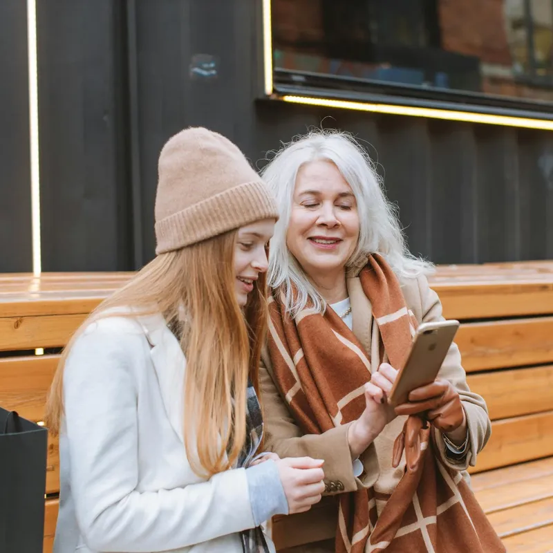 Woman and her mom looking at a phone outside and talking about the present perfect tense in English