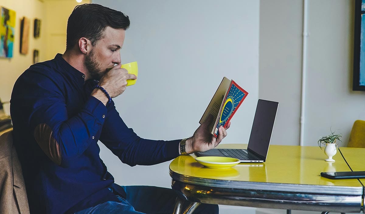 Man holding a book trying to find examples for the past continuous tense in there while drinking coffee
