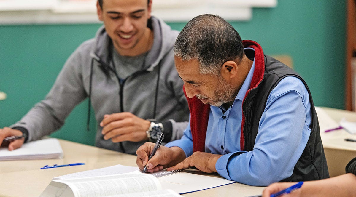 Man and his friend during an Italian class writing in a notebook