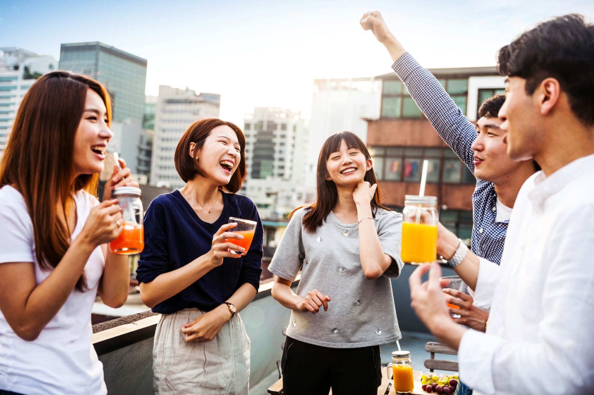 Friends on a rooftop smiling and laughing while celebrating with drinks in their hands