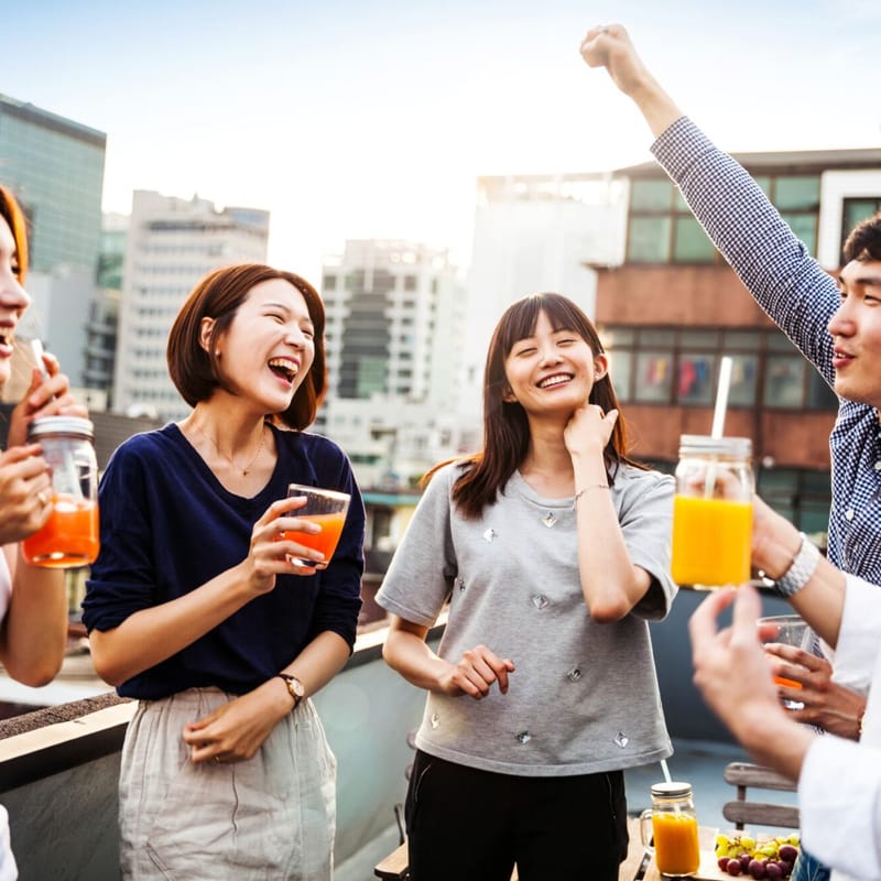 Friends on a rooftop smiling and laughing while celebrating with drinks in their hands
