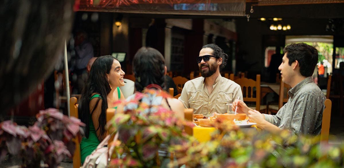 Friends sitting at a table in a restaurant and chatting while eating Latin-American food