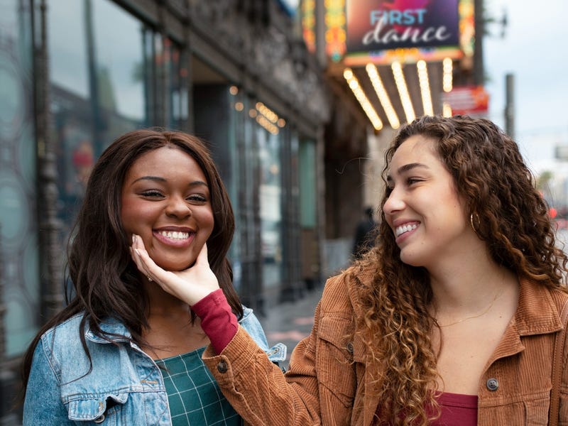 Woman holding the face of her friend who is speaking another language and laughing with her