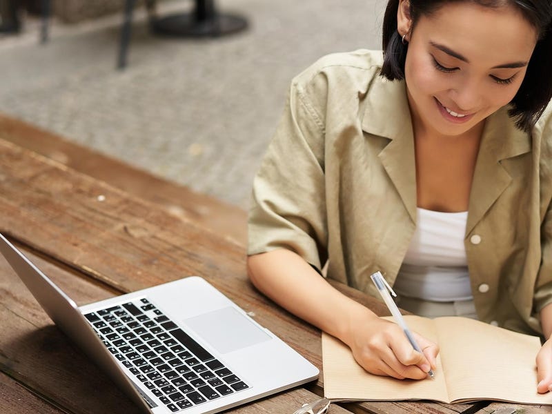 Woman in front of a laptop making notes while learning about French grammar rules