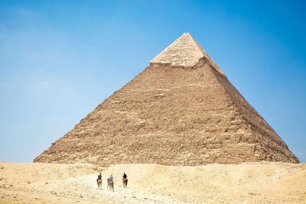 Visitors walking towards and Egyptian pyramid while talking to each other in Arabic