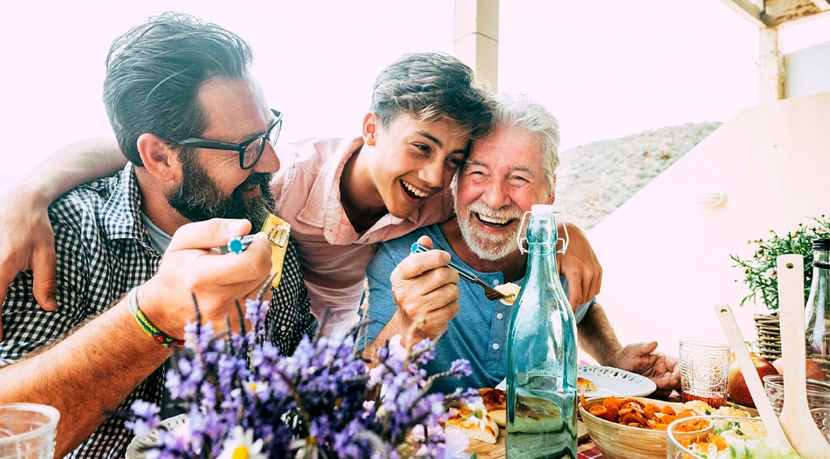 Grandfather, father and son hugging each other next to the dinner table