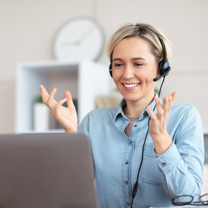 Woman in front of her laptop talking to her coworker and showing him Berlitz's online learning platform where she learns a language with a combination of a human instructor and AI