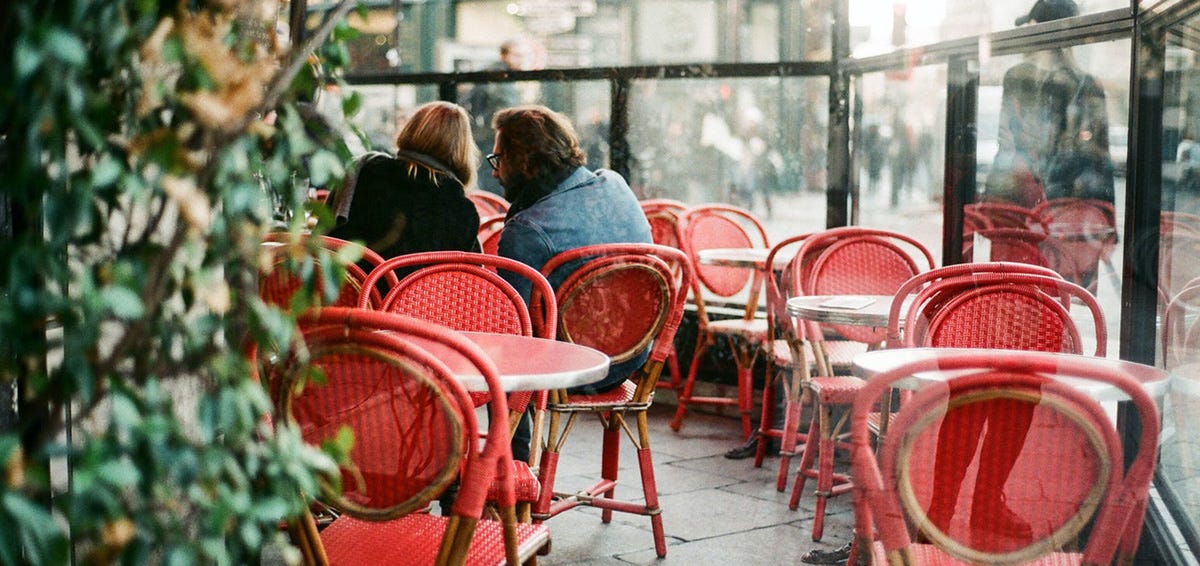 People sitting on red chairs and discussing what to order in a coffee shop