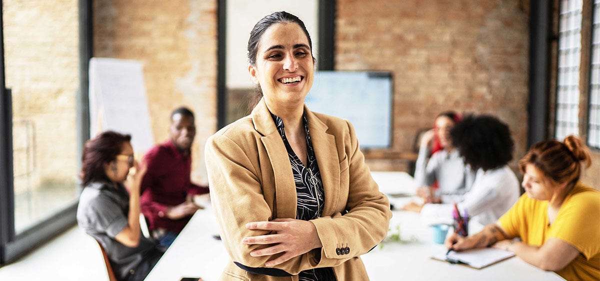 Woman standing in front of a desk and smiling proudly during a business meeting