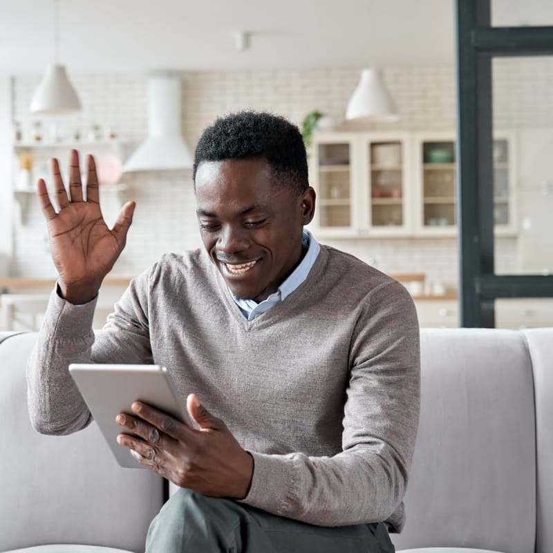 Man holding a tablet, waving and sazing hi to his isntructor at the beginning of his online English class with Berlitz