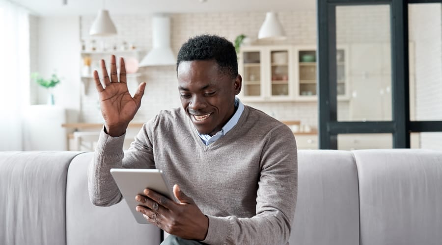 Man holding a tablet, waving and sazing hi to his isntructor at the beginning of his online English class with Berlitz