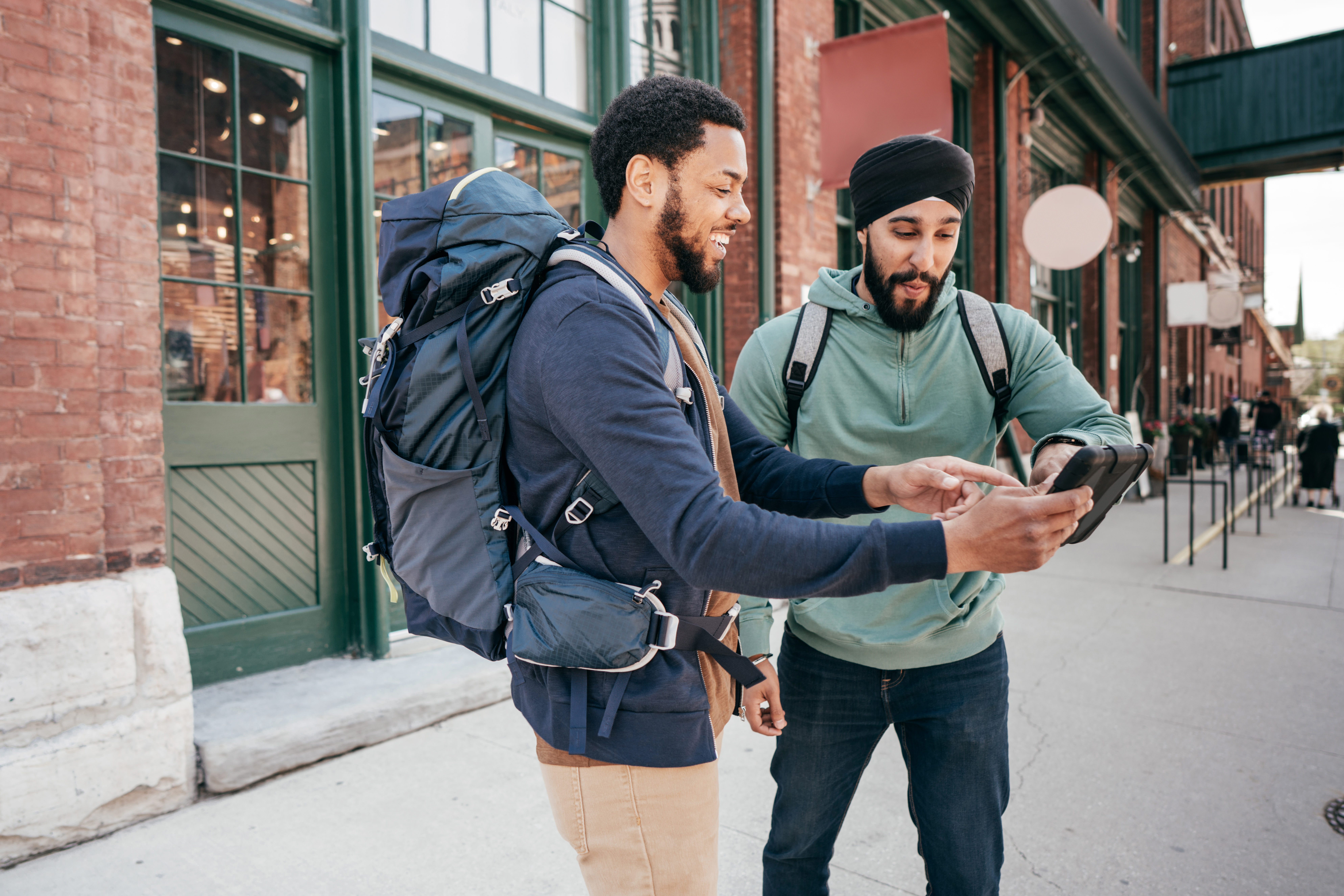 Two men on the street pointing at a phone and showing each other the English numbers