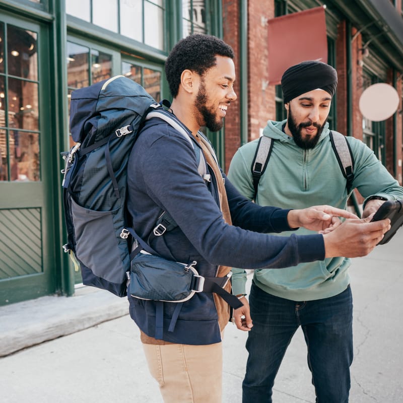 Two men on the street pointing at a phone and showing each other the English numbers