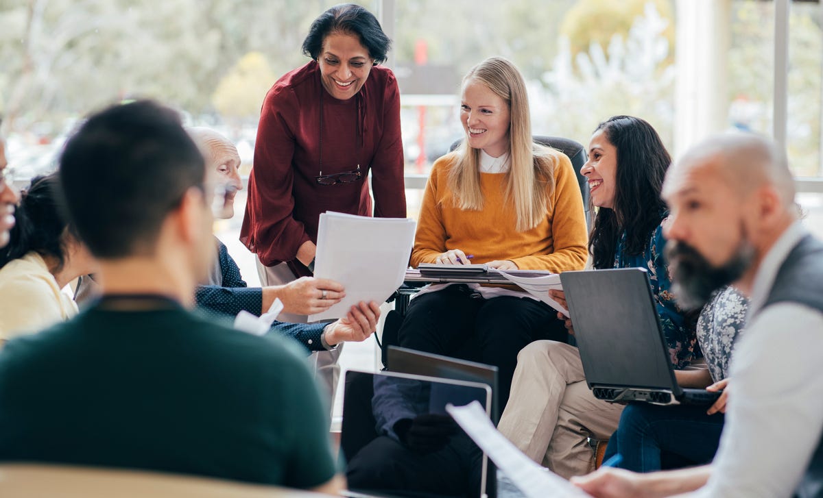 A group of students with laptops and papers and their instructor during an in-person language course for adults