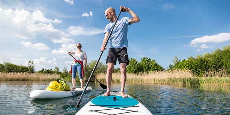 Ein Mann und eine Frau paddeln mit Touring-Boards und Gepäck nahe am See-Ufer