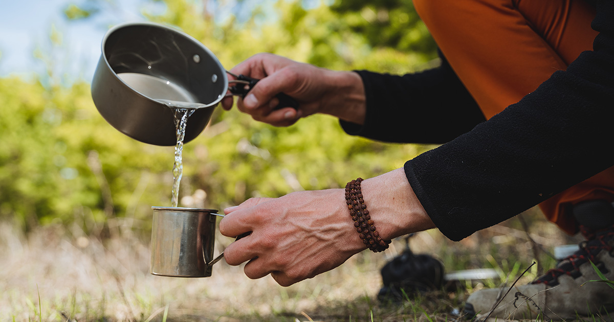 Un homme verse de l'eau d'une casserole dans un gobelet