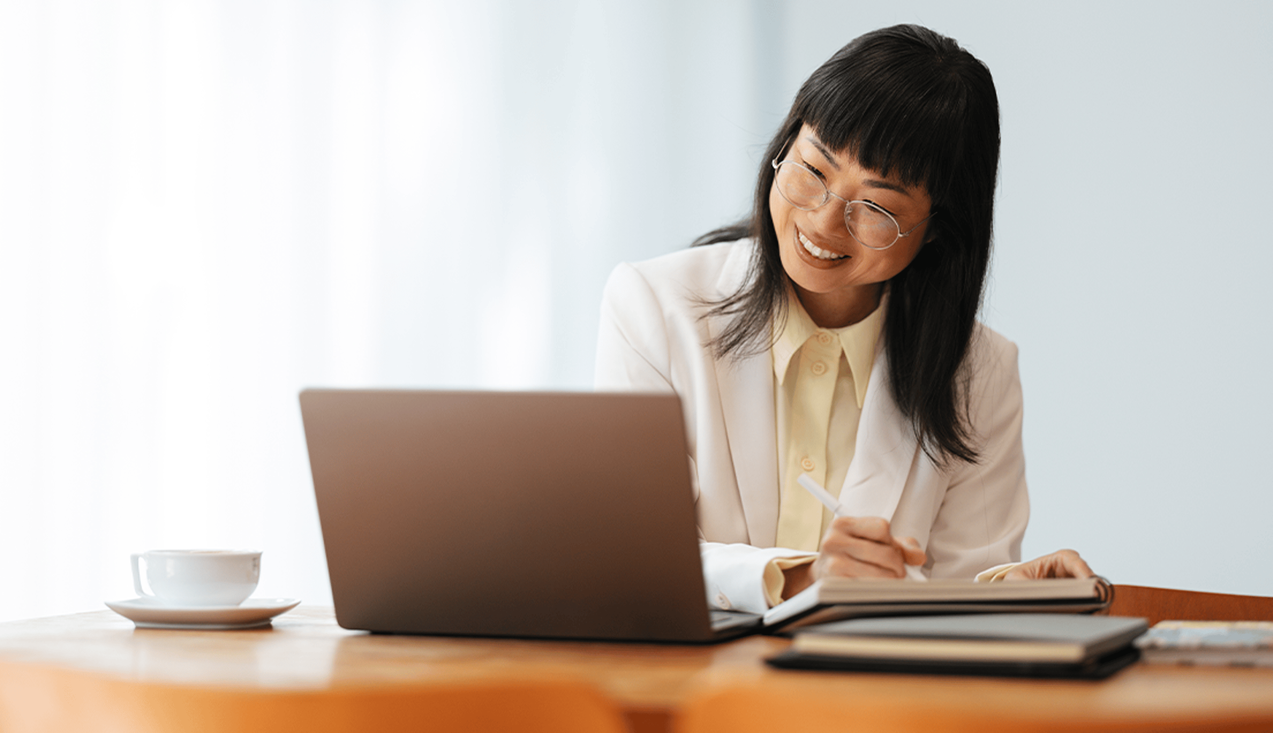 Woman Smiling at a Laptop and Taking Notes