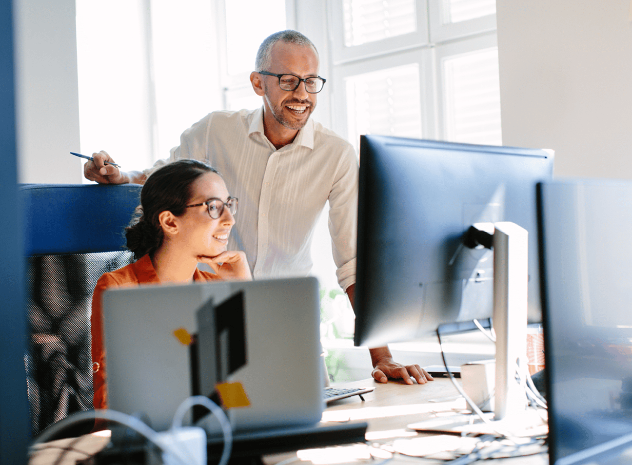 Two People in an Office Looking at a Computer and Smiling