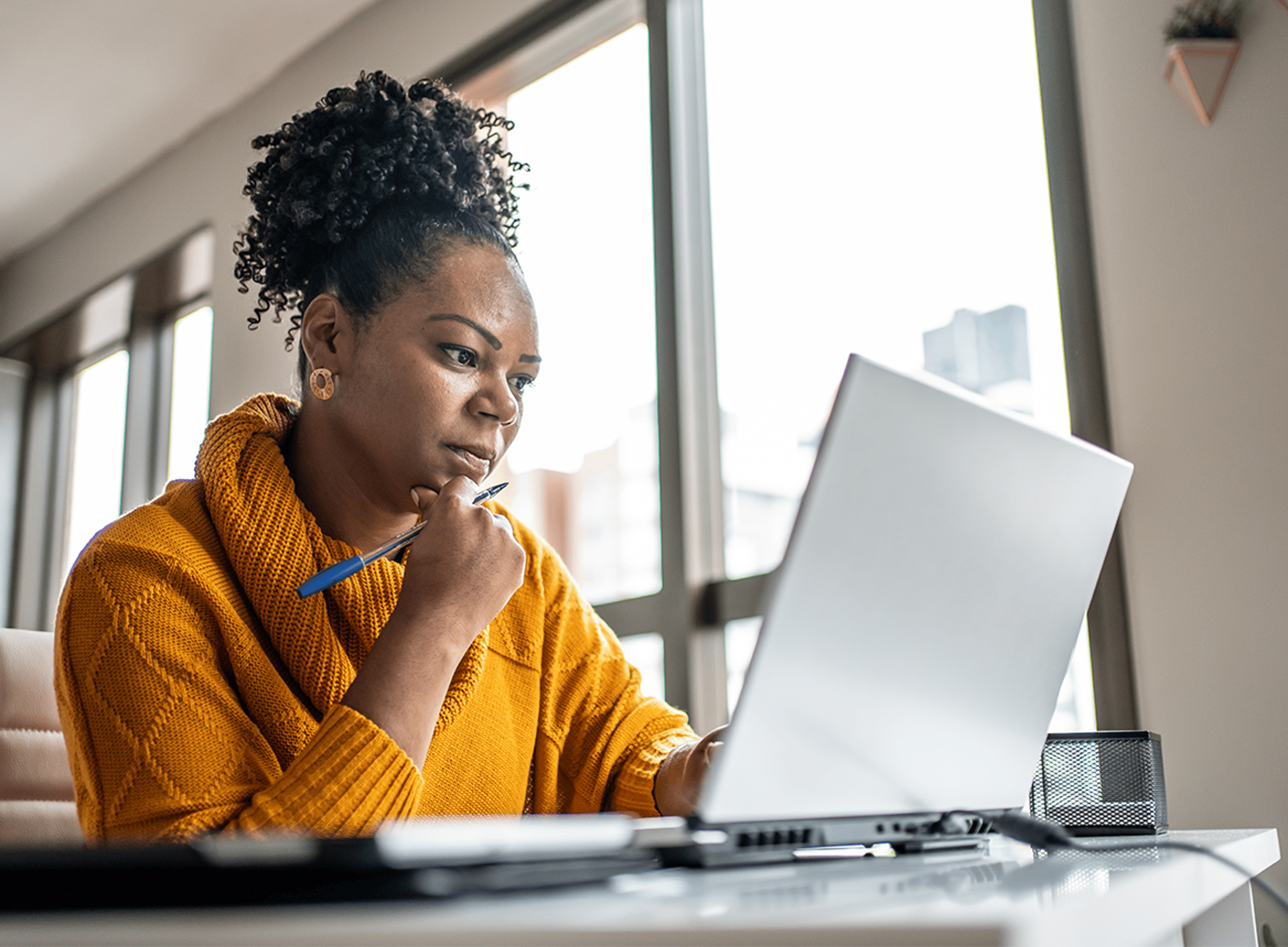 Woman Working at desk on laptop holding pen