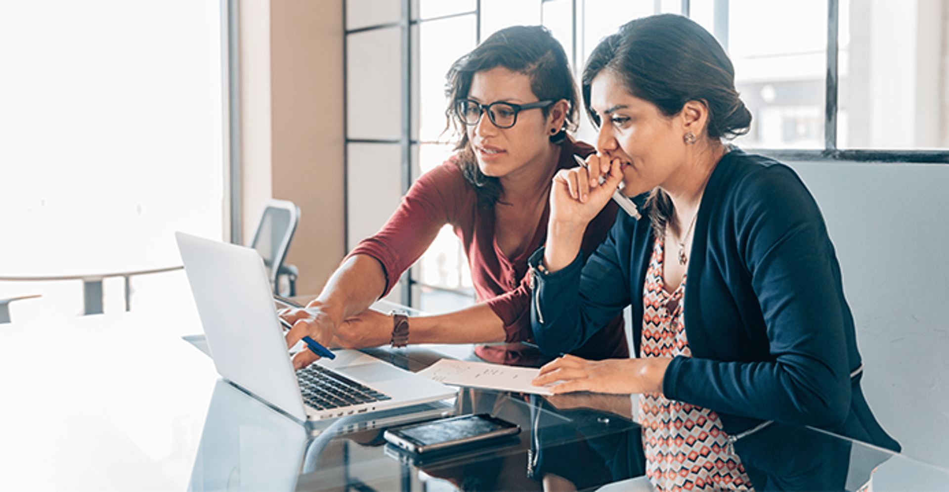 Two women working at a laptop making notes