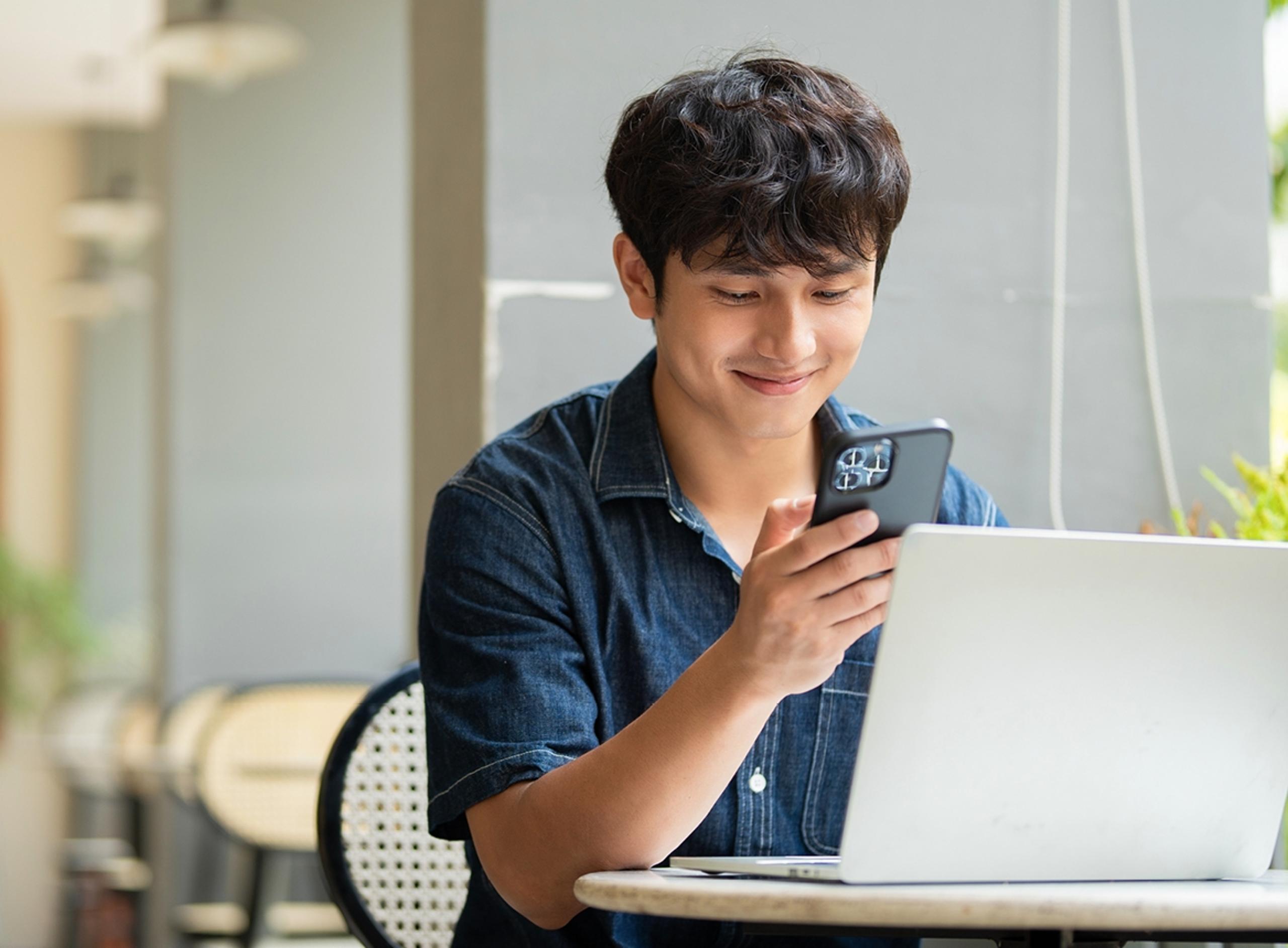 Man Smiling at His Phone While Using Laptop