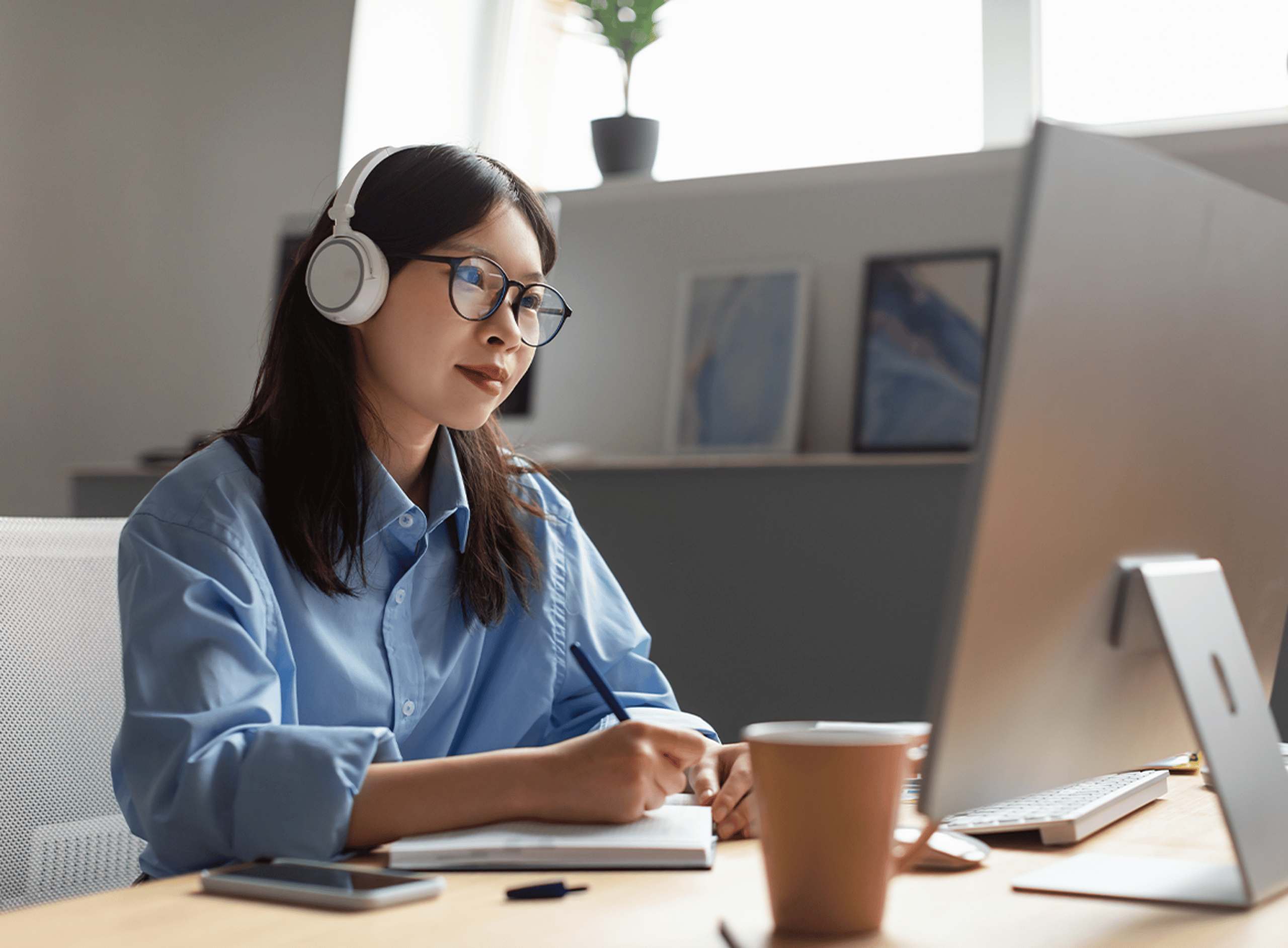 Woman studying from home writing on notepad with laptop with headphones on