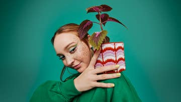 women in green dress holding a plant pot on her shoulder