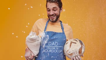 man wearing a denim apron holding a bag of flour and a loaf of bread