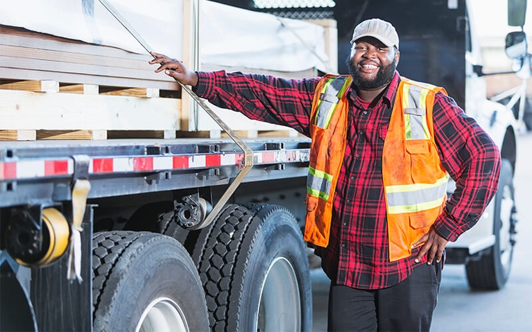 A trucking company owner poses with one hand resting on his flatbed trailer