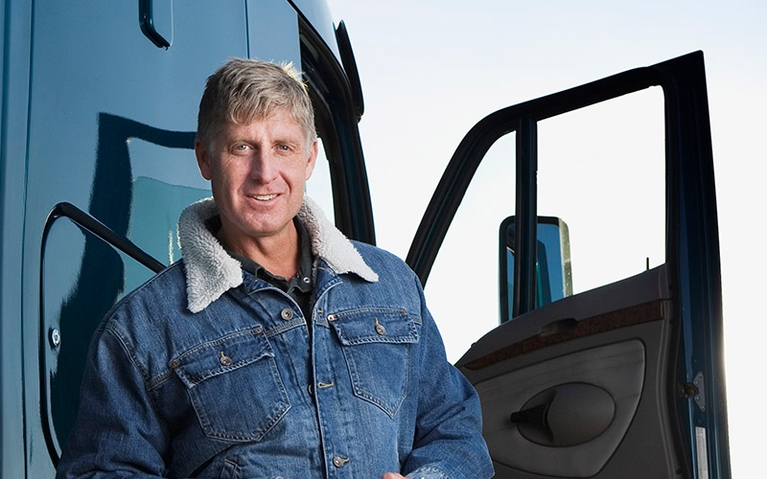 A man standing and smiling near a blue semi-truck.