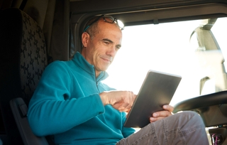 An owner-operator sits in his semi truck using a tablet to work on his business