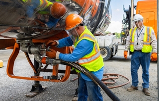 A tanker owner-operator attaches the hose to a tanker trailer while a Schneider trainer oversees in the distance