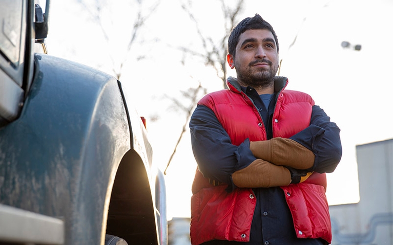 A man standing by a truck with his arms folded across his chest.