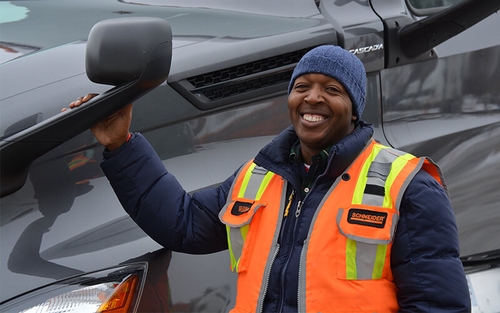 A Schneider owner-operator poses next to his truck with a hand resting on the sideview mirror