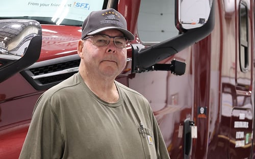 Owner-operator Michael Adams standing in front of a red semi-truck inside a shop.