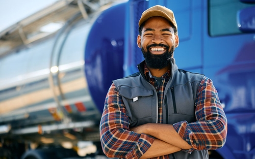 A man standing outside beside a tanker truck, smiling straight forward with his arms crossed.