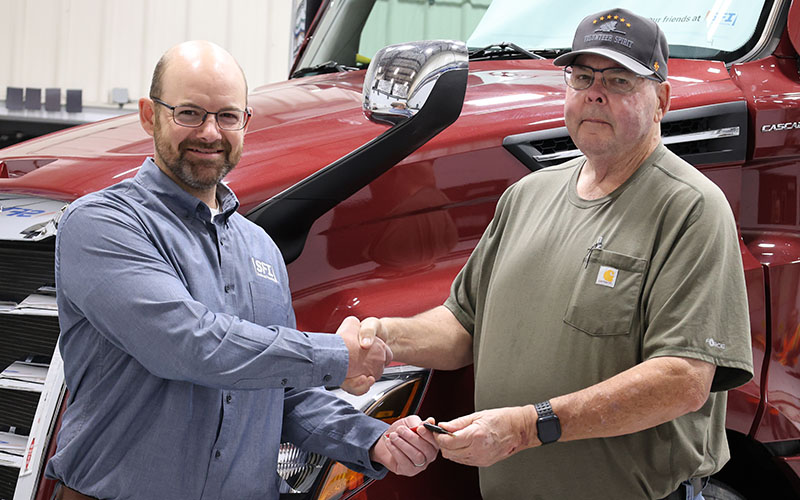Owner-operator Michael Adams shaking hands with an SFI Account Administrator. They are standing in front of a red semi-truck inside a shop.