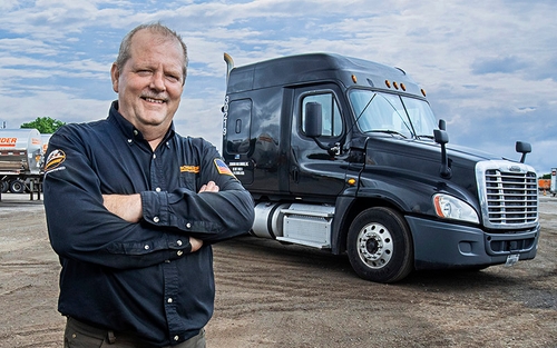 A Schneider owner-operator stands in front of a tanker truck with his arms crossed.