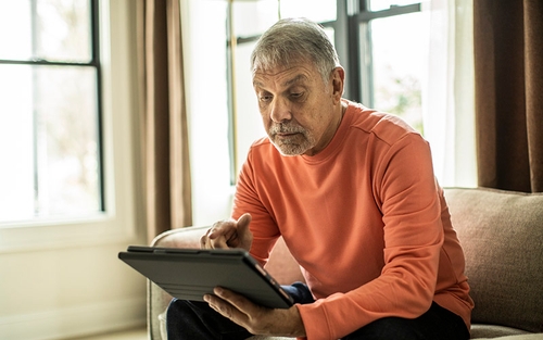 A man sitting on a couch and looking at a tablet.