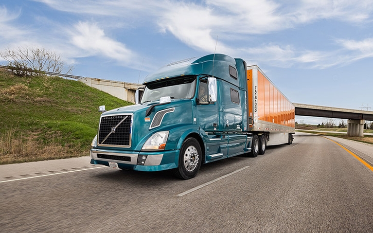 An owner-operator in a semi-truck hauls an orange Schneider van trailer down a country road