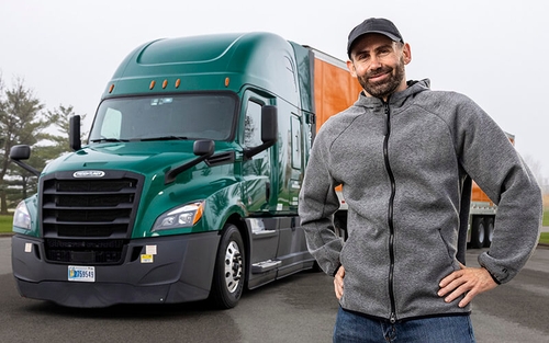 An owner-operator truck driver stands in front of his tractor which is hauling a Schneider trailer.