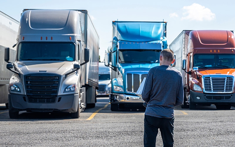 A man standing in front of several semi-trucks. 