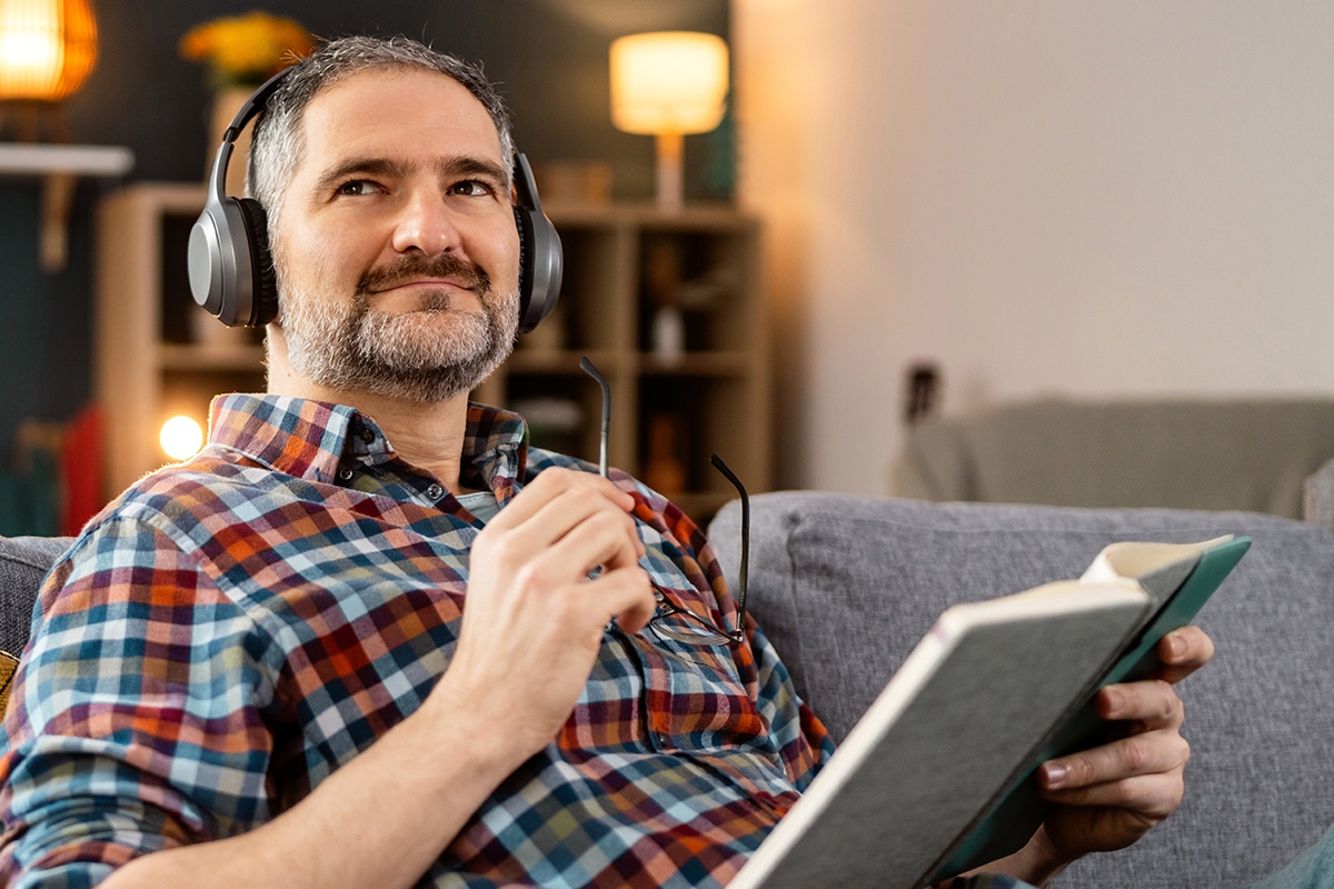 A man holding eyeglasses and wearing headphones