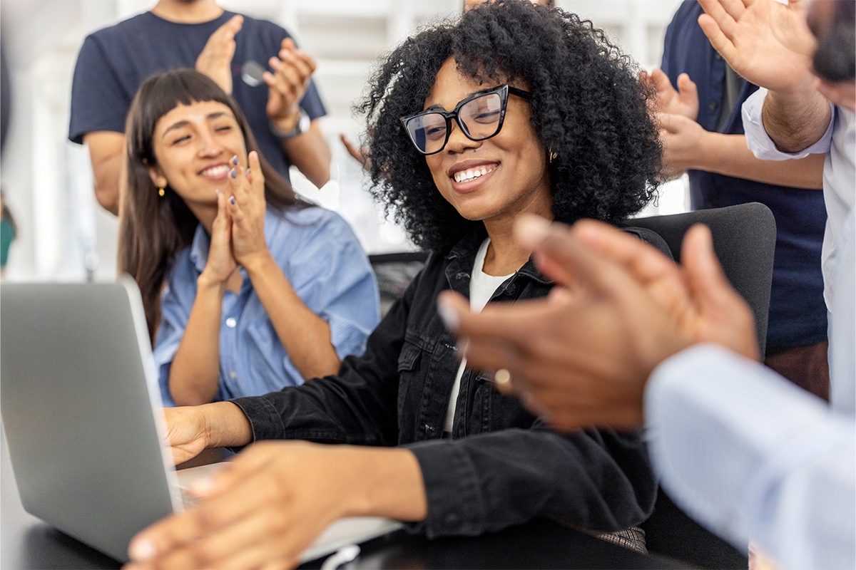 Woman with glasses smiling while others are clapping