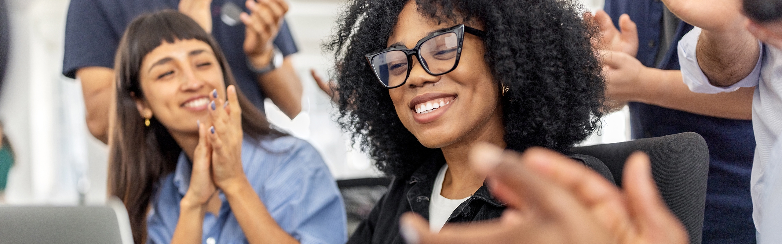 Woman with glasses smiling while others are clapping