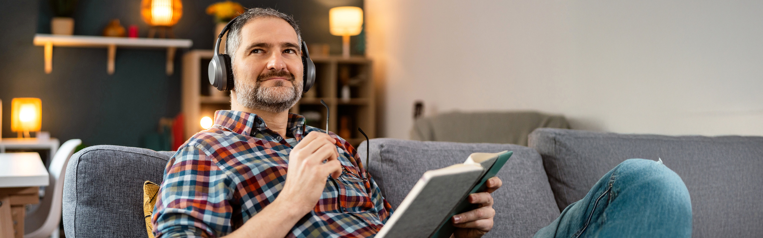 A man holding eyeglasses and wearing headphones