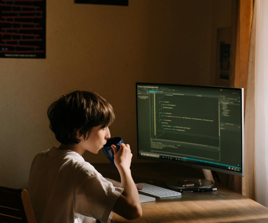 person sitting infront of monitor working and drinking coffee
