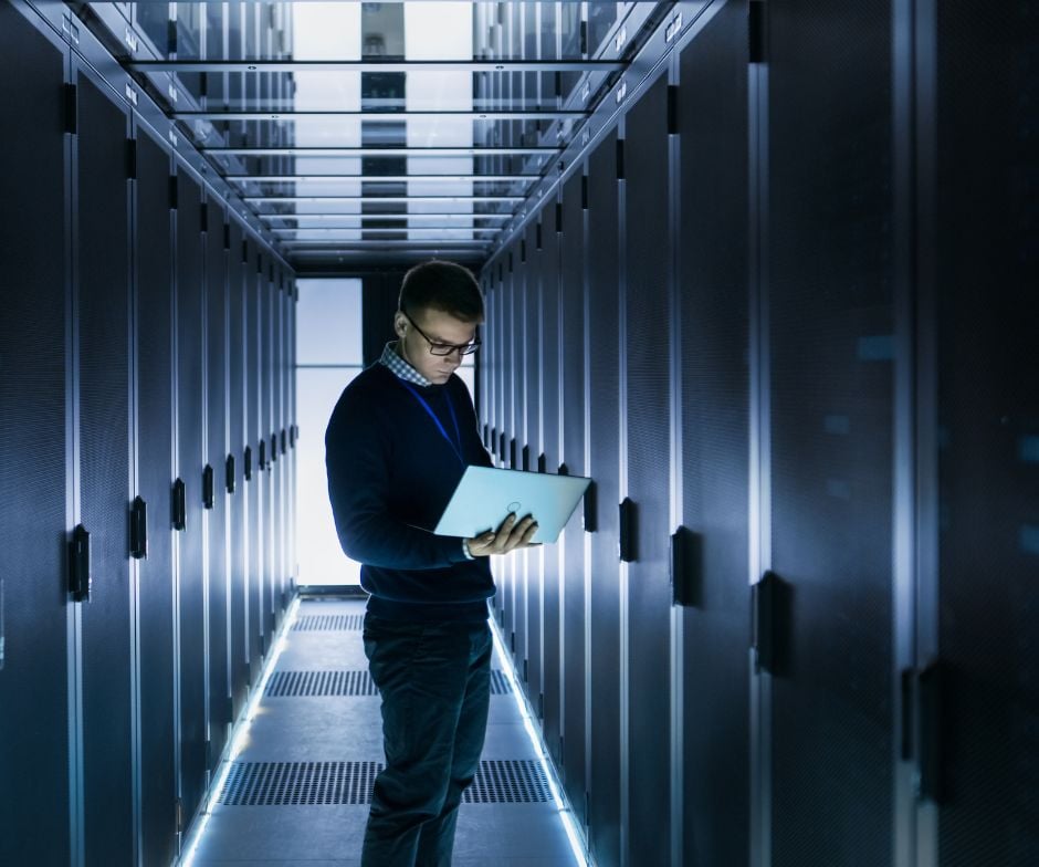 Person holding laptop and analyzing while standing inside data center